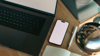 ノートPCとスマホ、メモ帳が並ぶシンプルな机の上