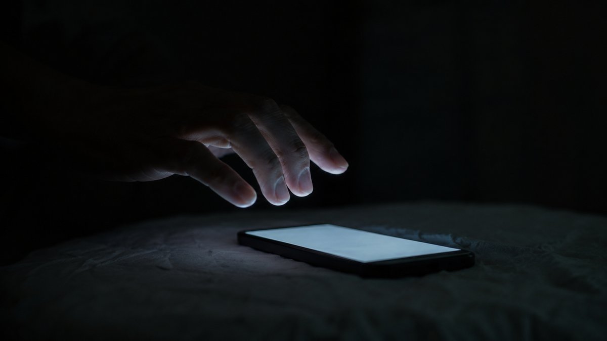 暗がりで光るスマートフォンにためらいながら手を伸ばす様子